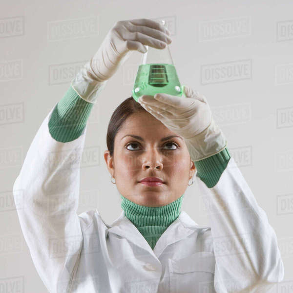Indian female scientist looking at beaker of liquid Stock Photo