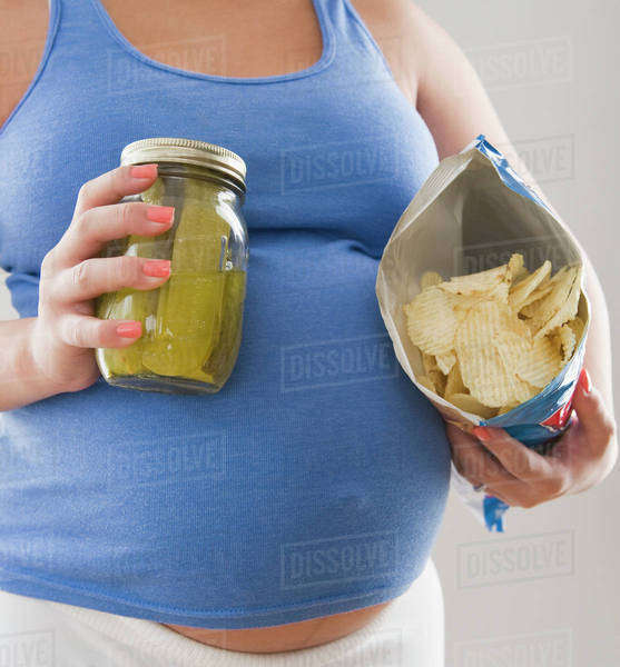 Pregnant Hispanic woman holding pickles and potato chips Stock Photo