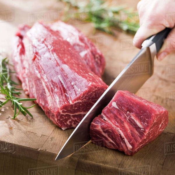 Knife cutting beef tenderloin on wooden table Stock Photo Dissolve