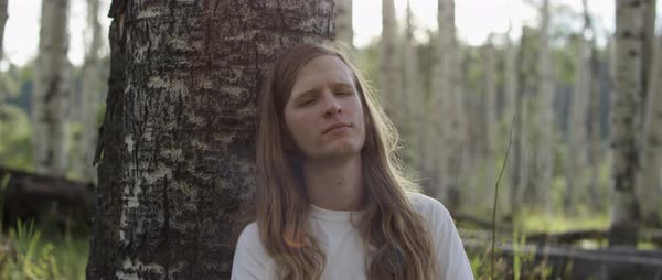 Portrait Of A Sad Young Man With Very Long Hair Leaning On Tree