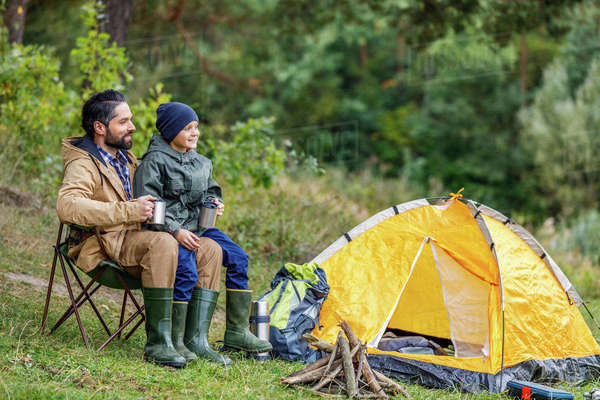 Happy father and son sitting in camping with tent in forest - Stock