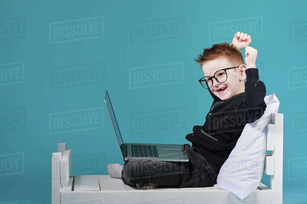 schoolboy-in-glasses-using-laptop-sitting-on-bed-happy-child-doing