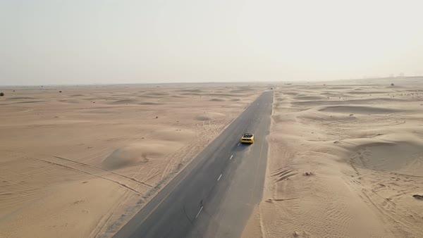 A yellow car is driving along an asphalt road in the desert, raising sand dust behind it. Drone Video - 4K Royalty-free Stock Video Footage | Dissolve