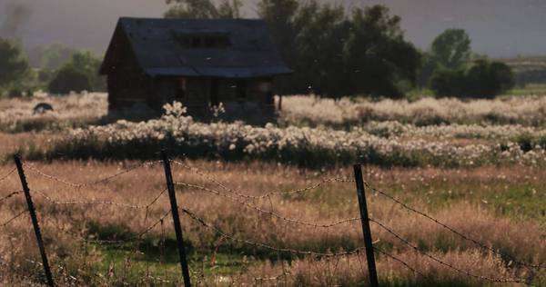 An Old Cabin Sits Behind A Fence In A Beautiful Mountain Meadow