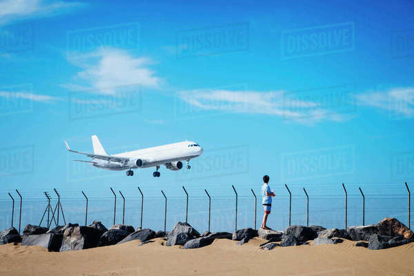 Boy On Beach Watching Airplane Flying Low In Blue Sky Near Lanzarote 