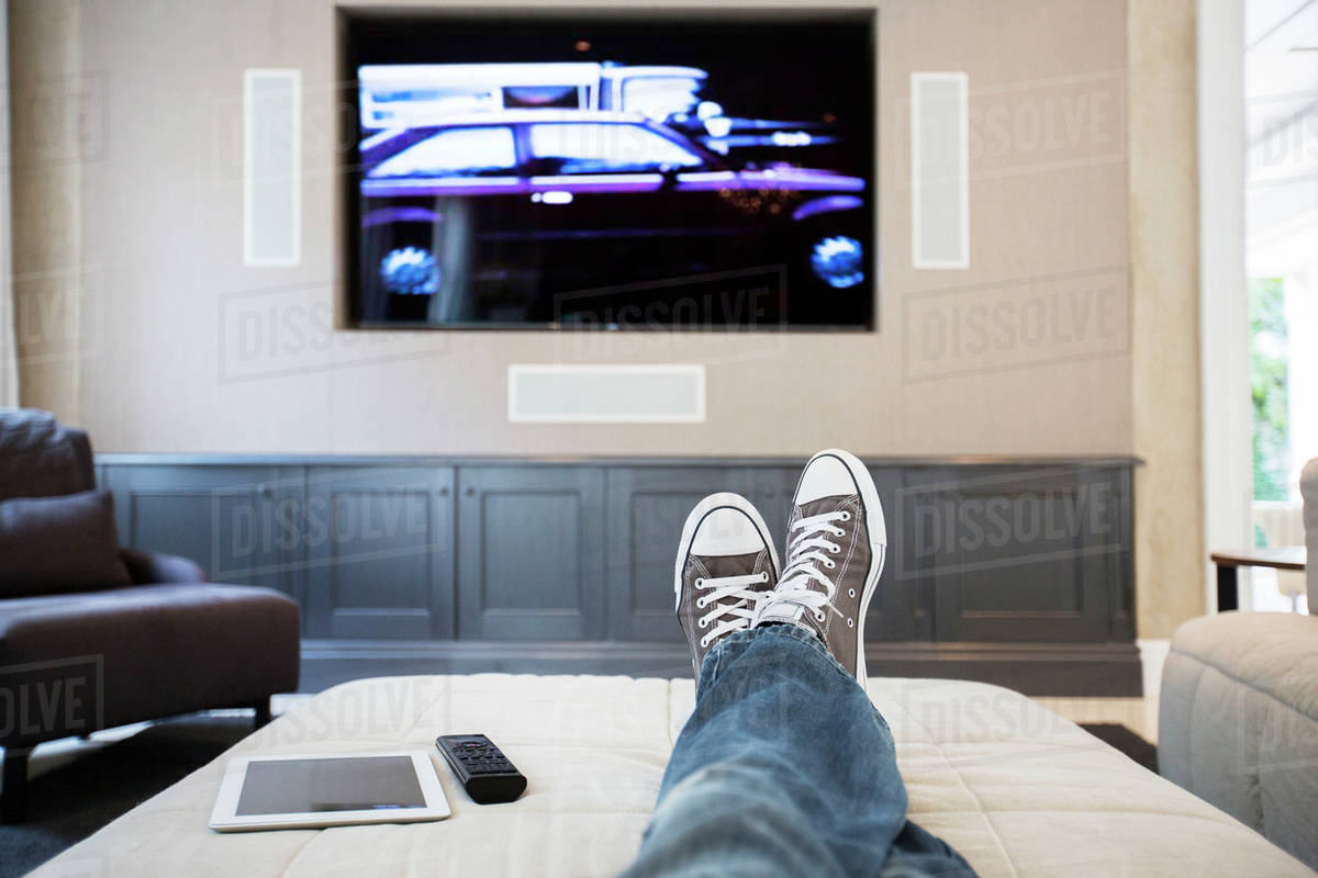 Woman's feet on ottoman watching TV Stock Photo Dissolve