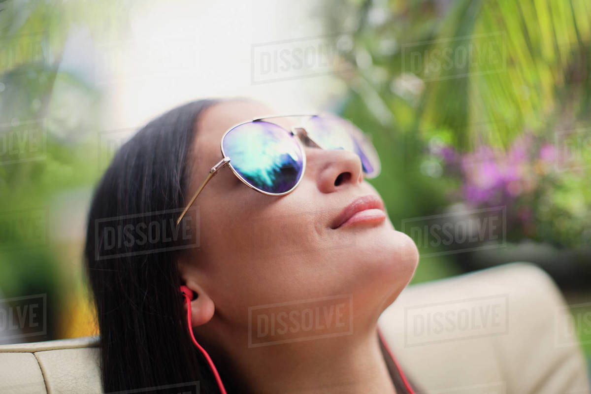 Close up serene woman in sunglasses sunbathing, listening to music with