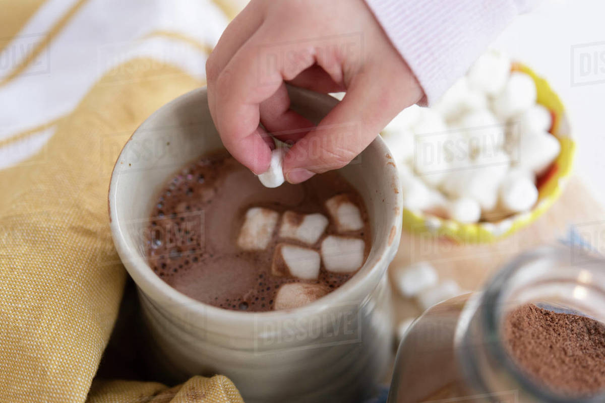 Girl's hand putting marshmallows in hot chocolate Stock Photo Dissolve