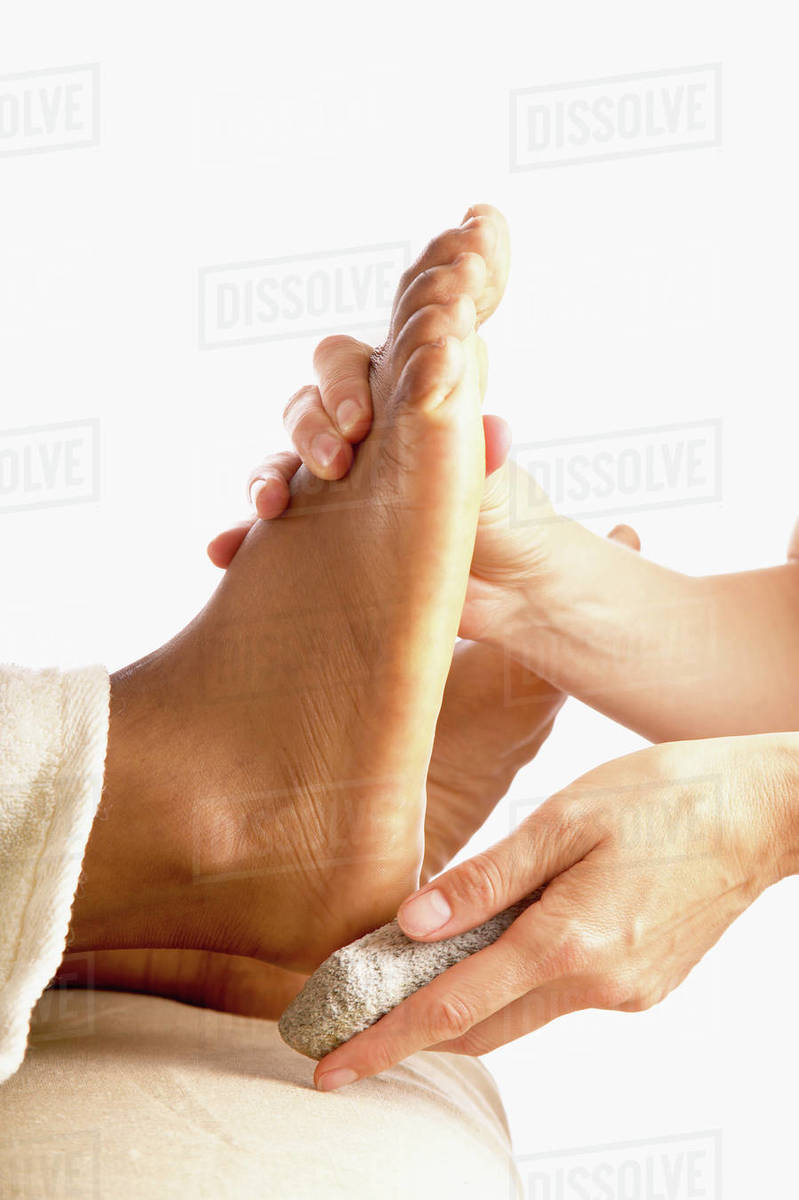 Closeup of hands using pumice stone on foot Stock Photo Dissolve