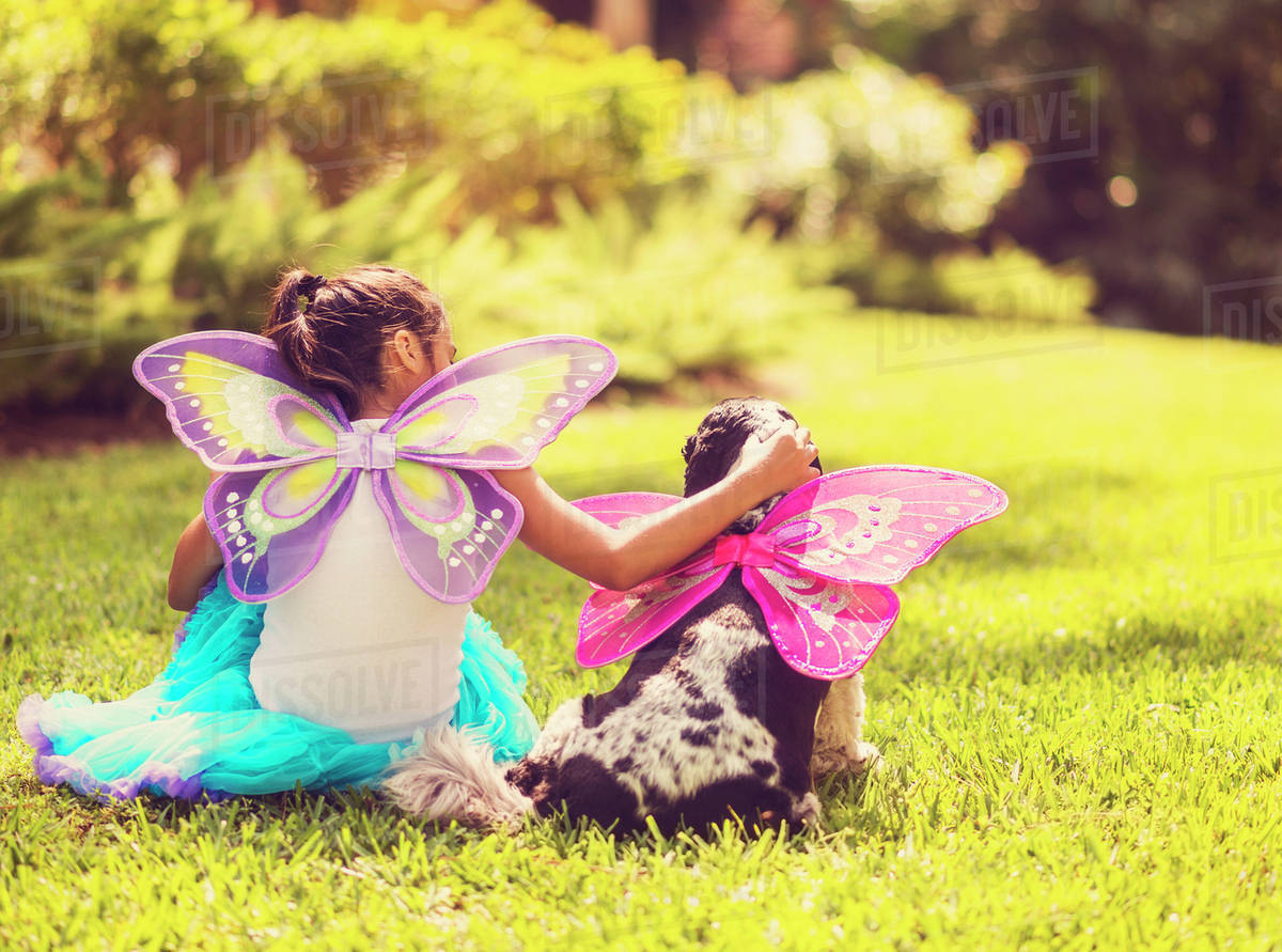 Rear view of girl (8-9) wearing fairy costume stroking dog Royalty-free stock photo