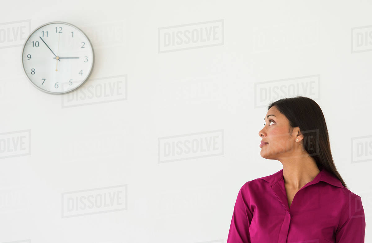 Woman looking at clock on wall Stock Photo Dissolve