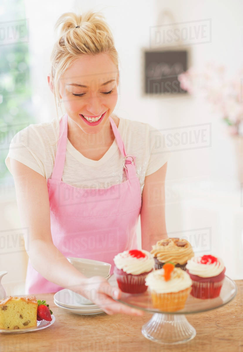 Smiling young woman in apron holding cake stand Stock Photo Dissolve