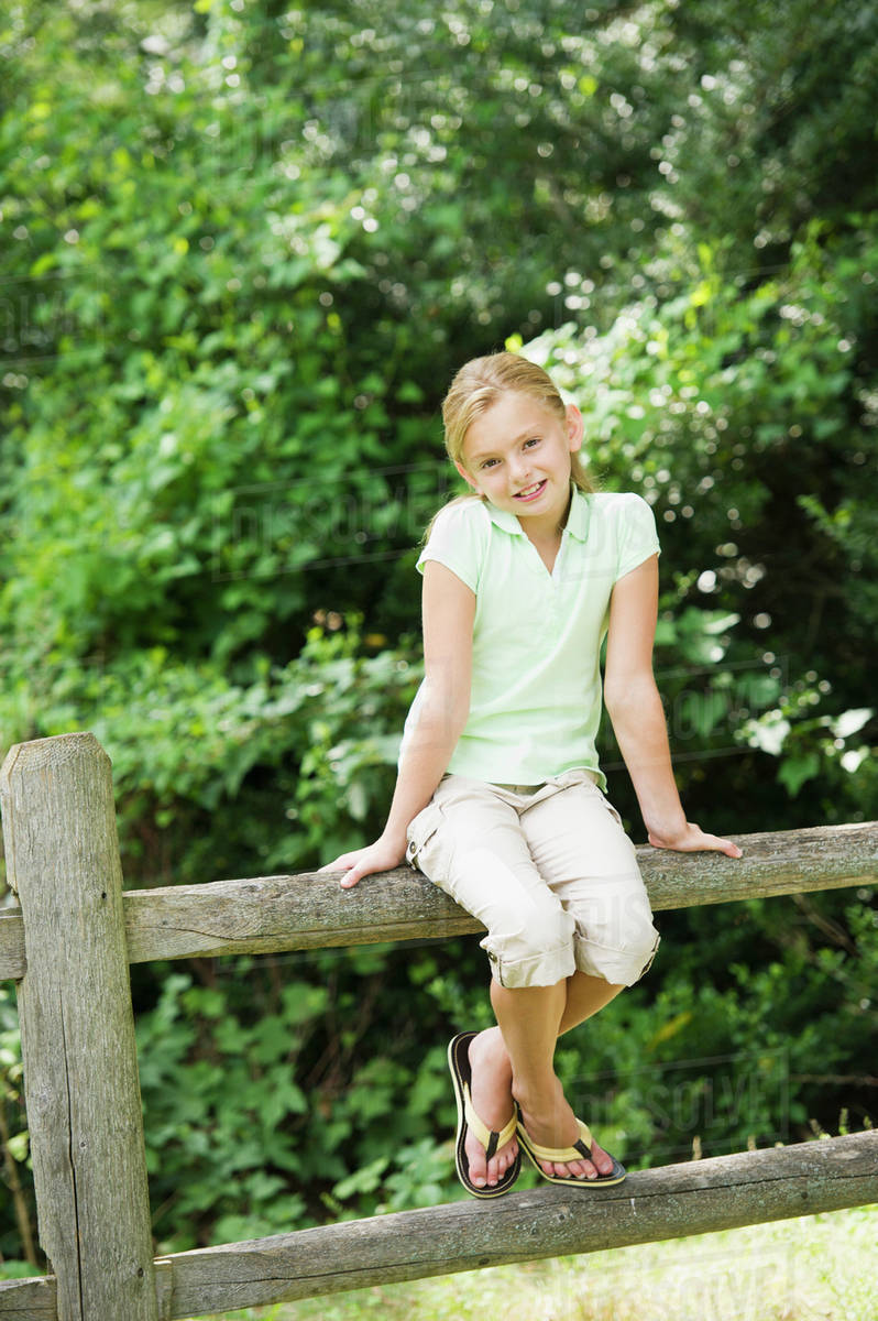 Smiling girl (10-11) sitting on fence - Royalty-free Stock Photo | Dissolve