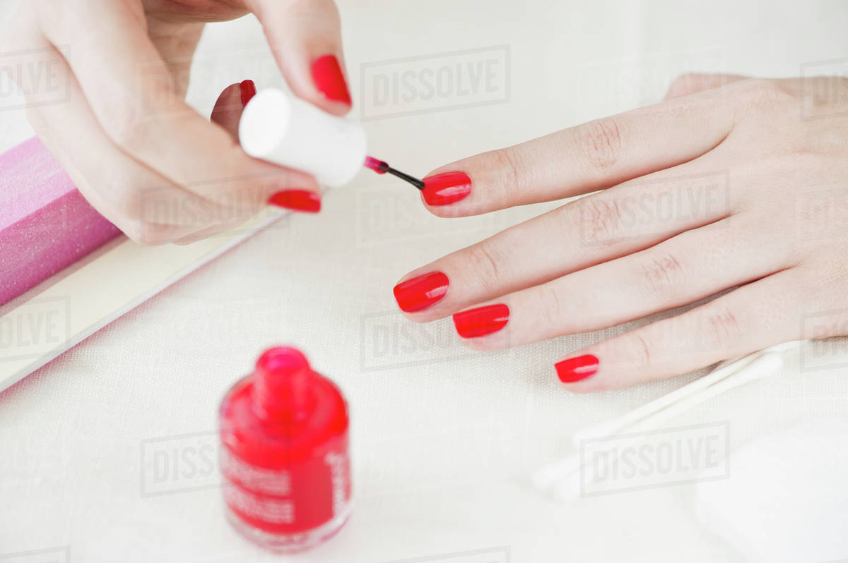 Woman painting her nails with red nail polish Stock Photo Dissolve
