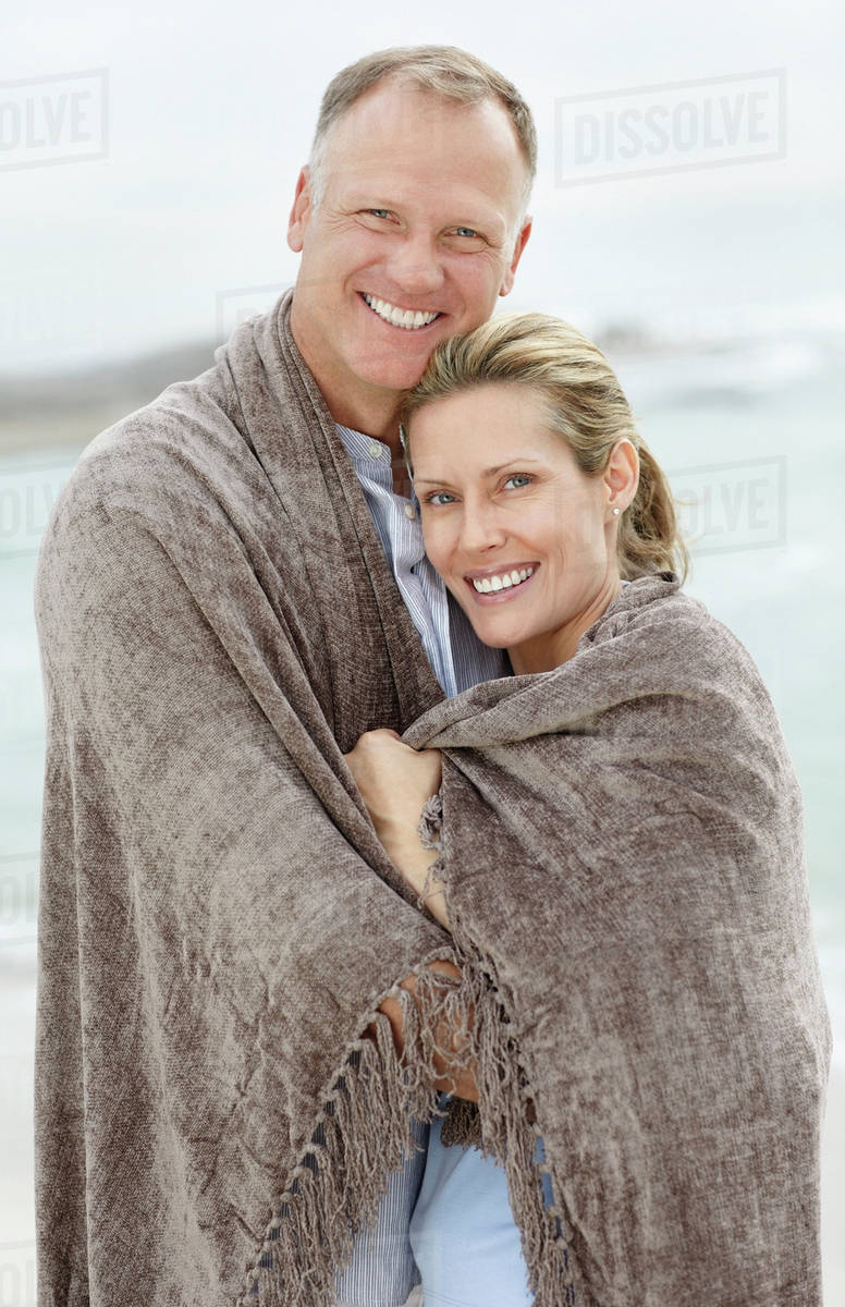 Portrait of couple wrapped in blanket on beach Stock Photo Dissolve