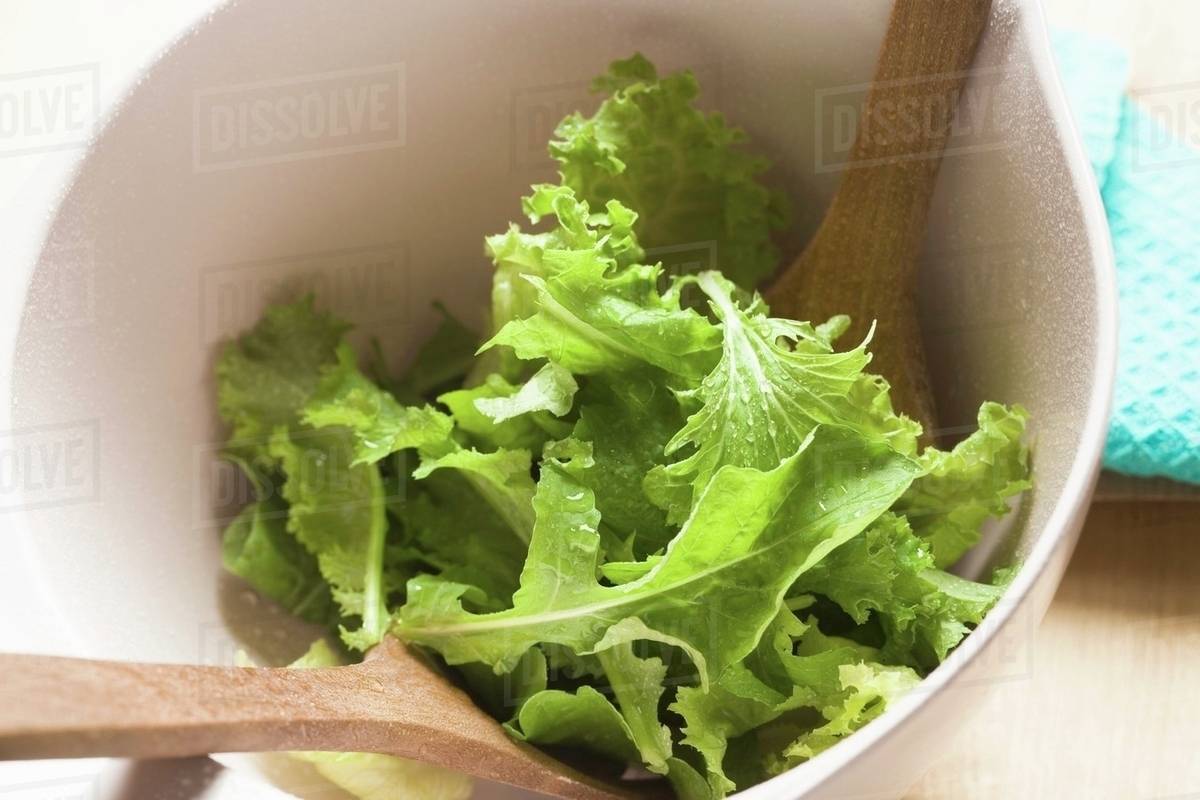Mixed salad leaves in bowl with salad servers Stock Photo Dissolve