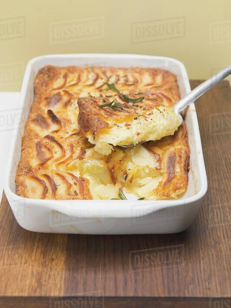 Potato gratin in baking dish with piece on server Stock Photo Dissolve