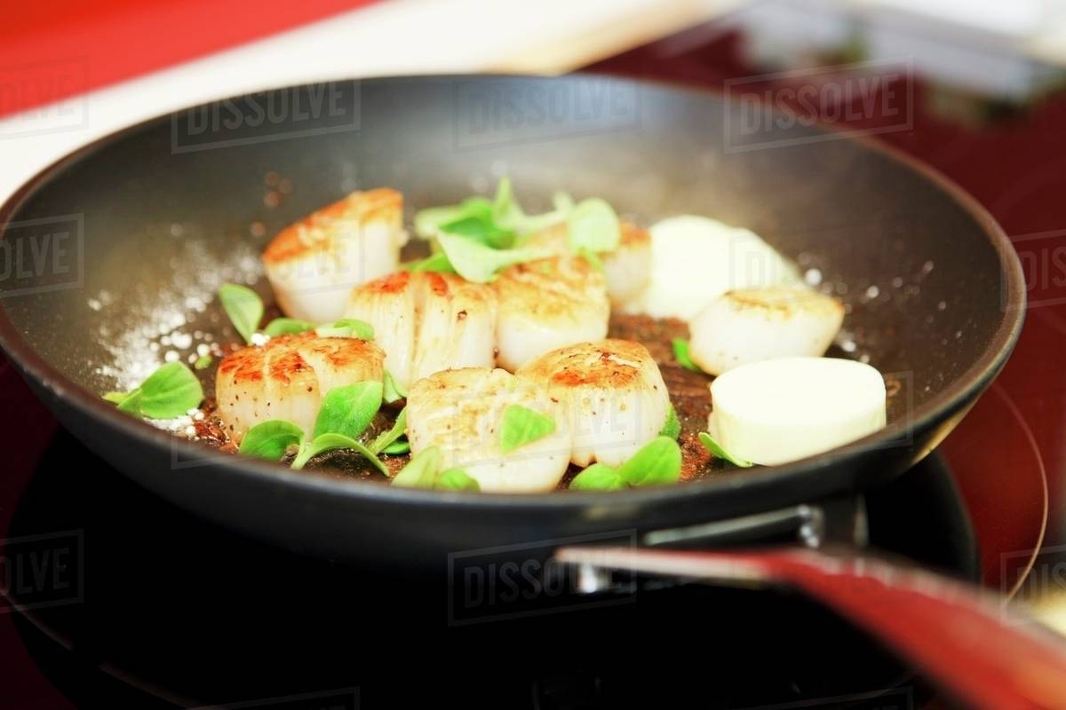 Scallops with field thyme, sea salt and butter being fried in a pan