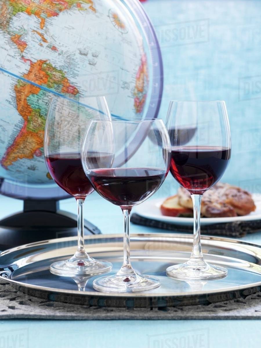 Three glasses red wine on a silver platter in front of a globe -  Royalty-free Stock Photo | Dissolve