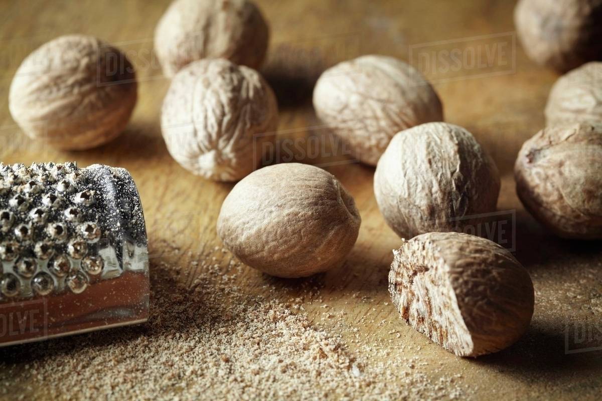Nutmeg, whole and grated, with a nutmeg grater Stock Photo Dissolve
