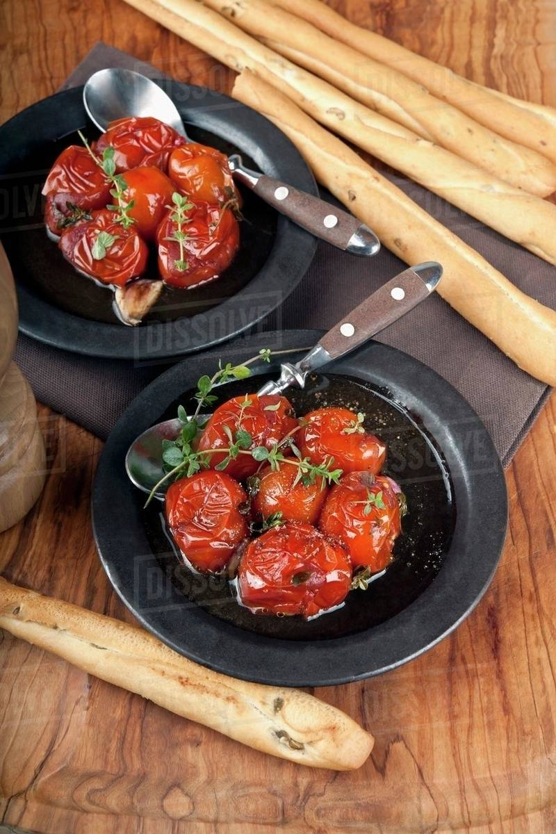 Confit tomatoes in olive oil with lemon thyme and balsamic vinegar and olive bread sticks on a