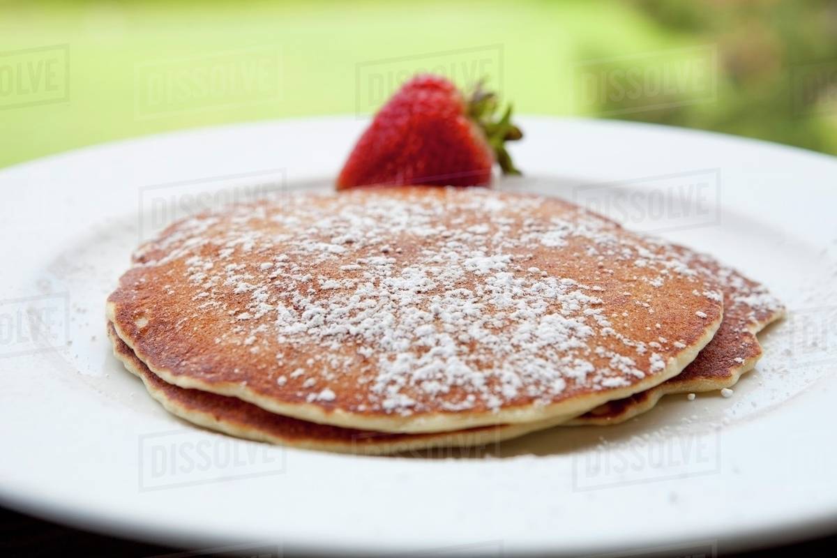 Pancakes with Powdered Sugar and a Strawberry; Outdoors Stock Photo Dissolve