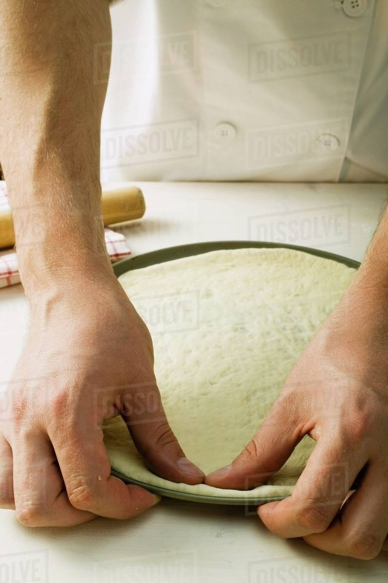 Pressing pizza dough into baking tin Stock Photo Dissolve