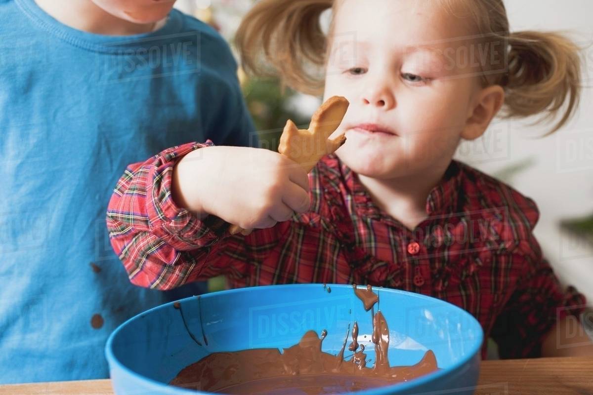 Girl dipping Christmas biscuit in chocolate icing Stock Photo Dissolve