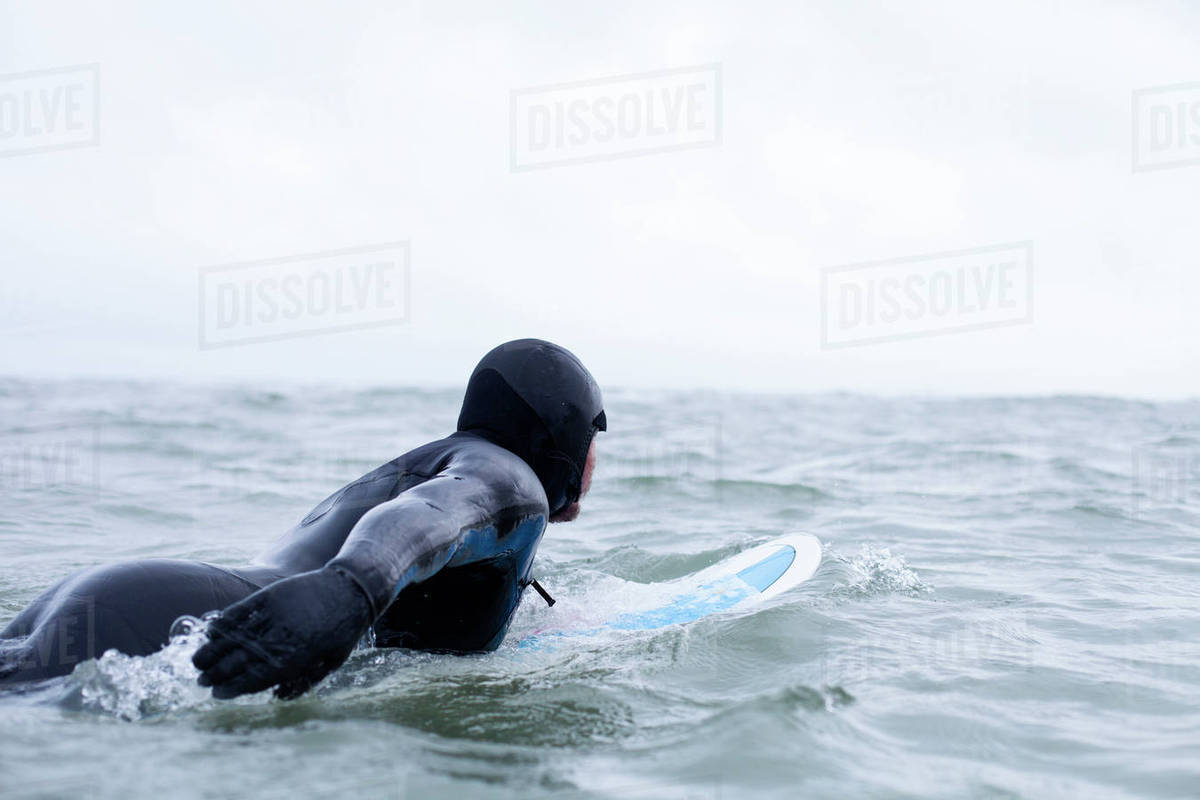 Surfer wearing wetsuit floating with board in wintery sea Stock Photo