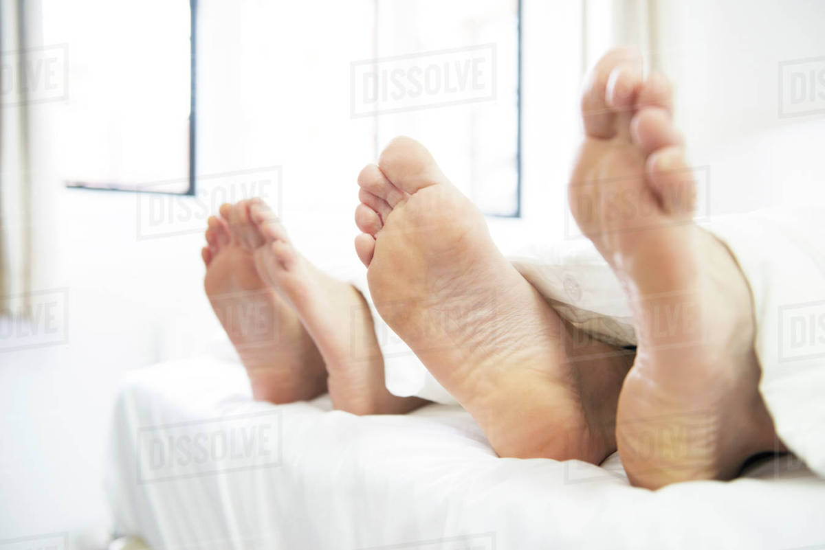 A couple lying in a bed with their feet sticking out from underneath