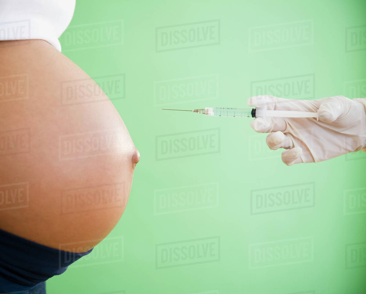 Gloved hand pointing needle at pregnant woman's stomach Stock Photo