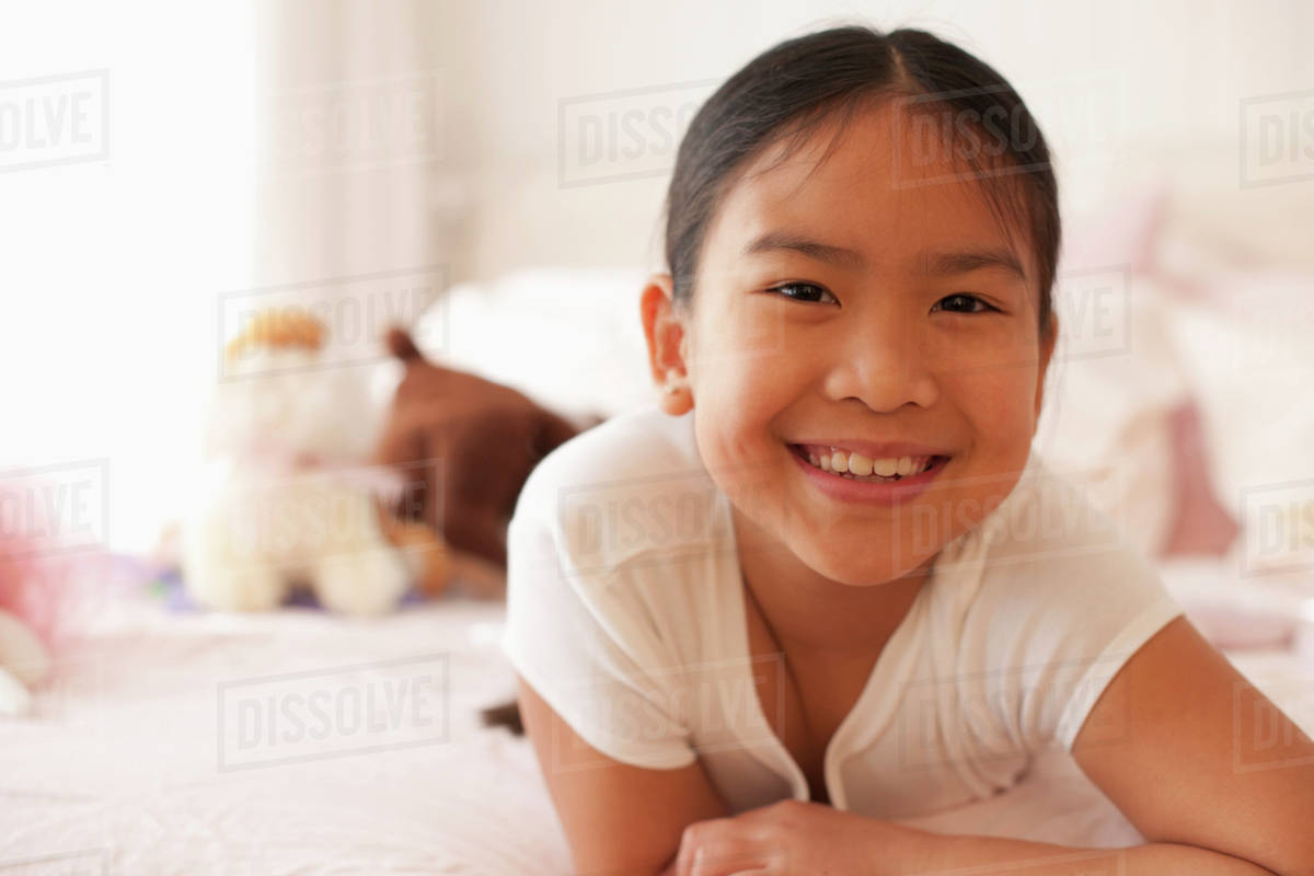 Smiling Asian girl laying on bed Stock Photo Dissolve