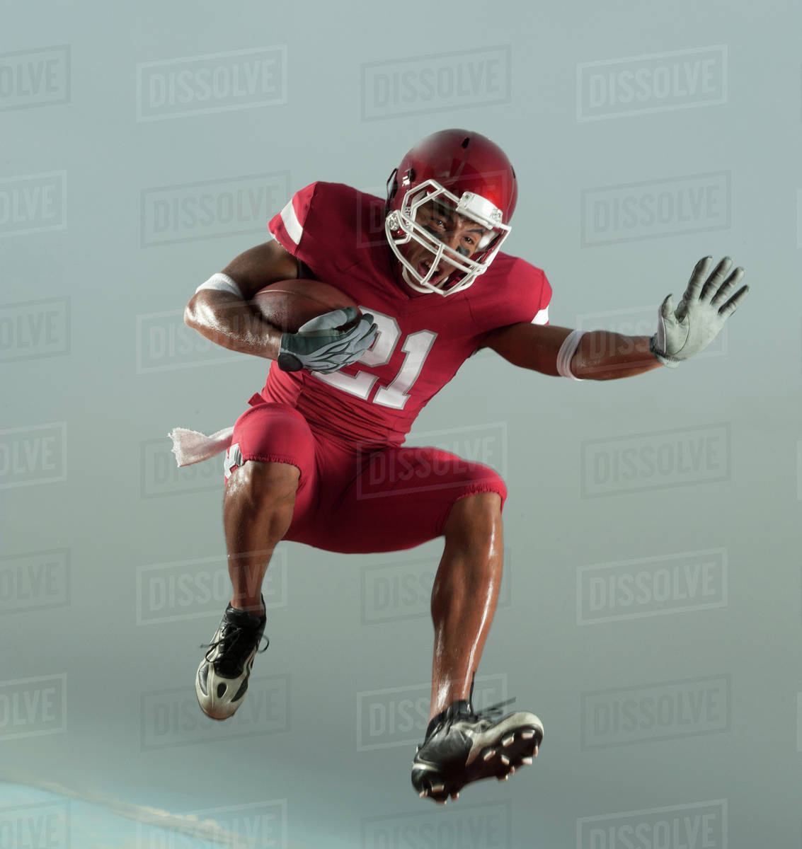 Grimacing Black football player carrying football in midair Stock
