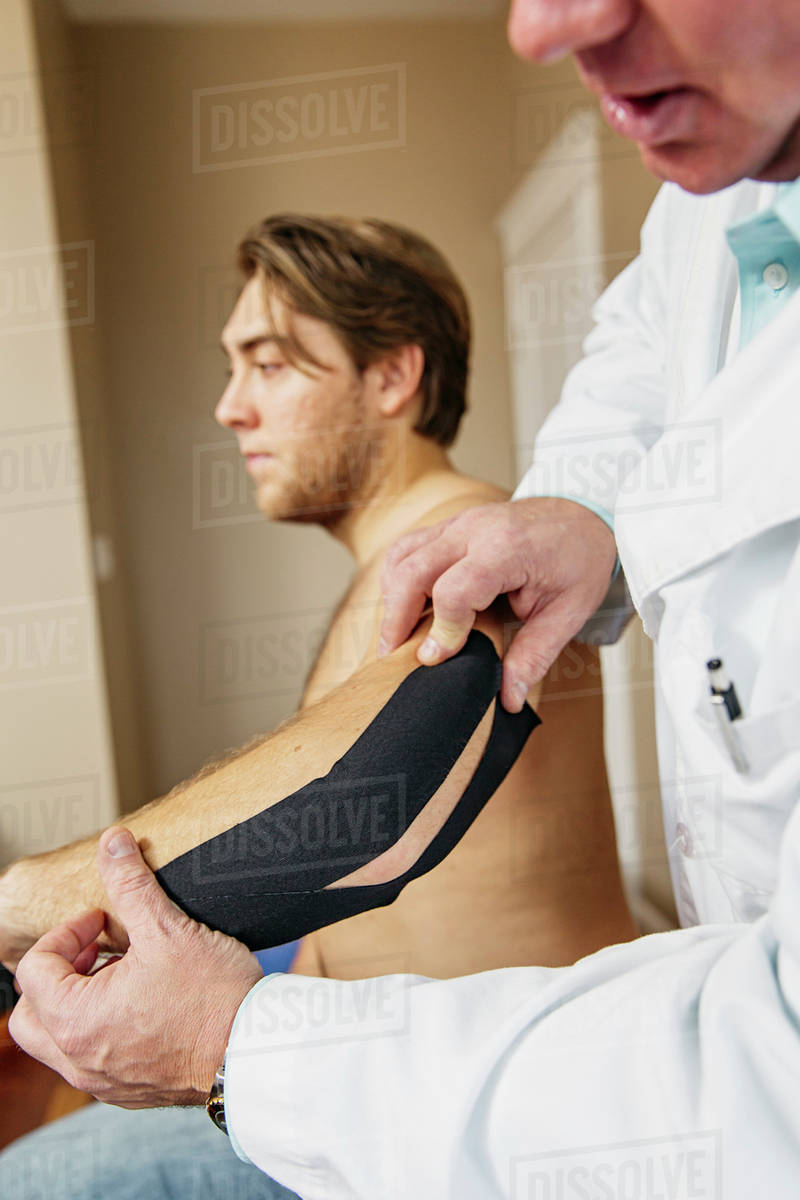 Caucasian doctor applying tape to elbow of patient Stock Photo Dissolve
