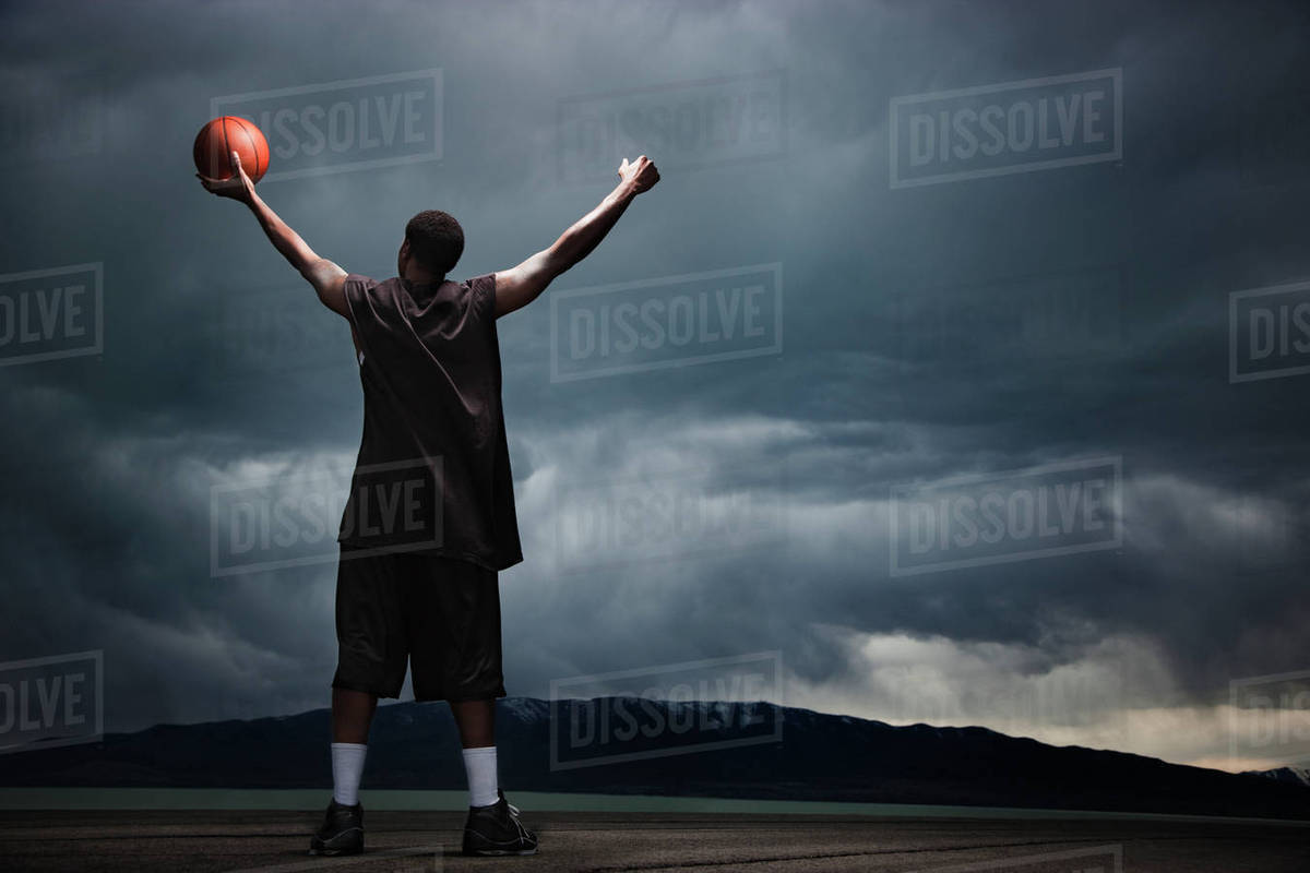 Mixed race basketball player standing with storm clouds in distance