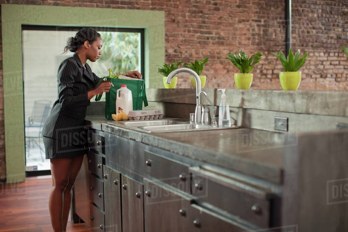 Mixed race woman unloading groceries in kitchen Stock Photo Dissolve