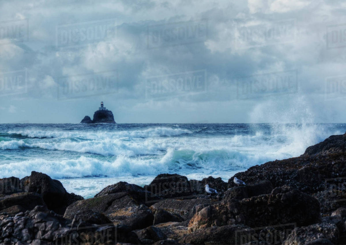 Waves crashing on rocky beach with lighthouse in distance, Tillamook