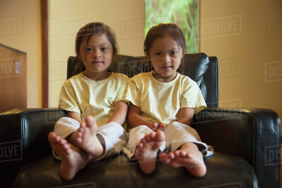 Mixed race twins with Down syndrome sitting in armchair Royalty