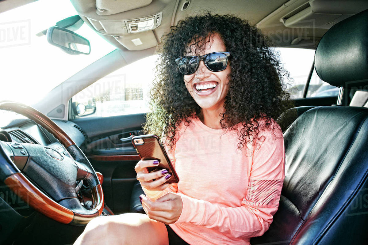 Laughing Hispanic woman in car holding texting on cell phone Royalty-free stock photo