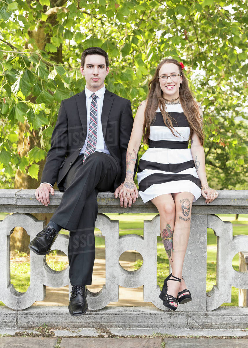 Welldressed Caucasian couple sitting on wall at park Stock Photo