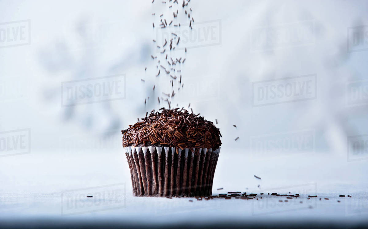 Brown sprinkles falling on chocolate cupcake Stock Photo Dissolve