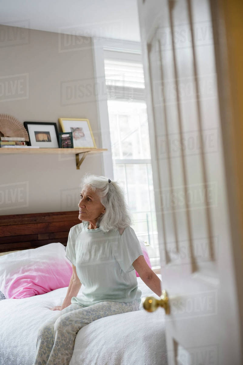 Older woman sitting on bed beyond doorway - Stock Photo - Dissolve
