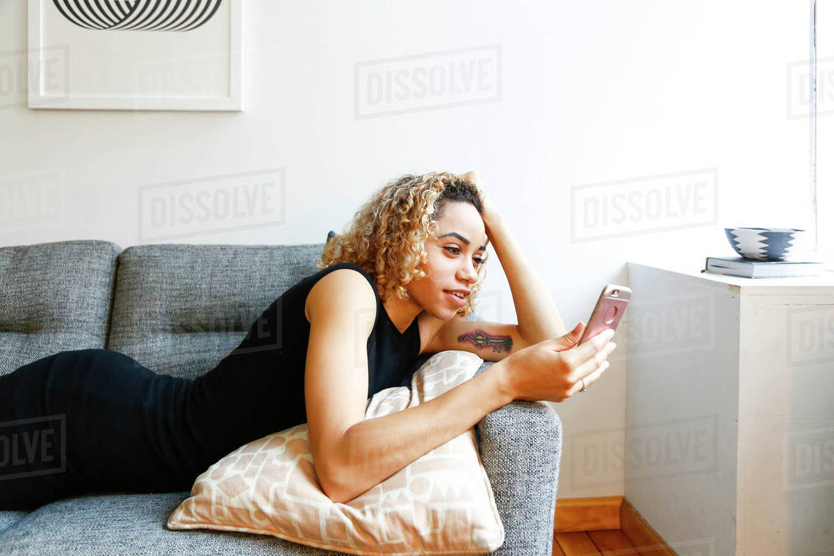 Mixed Race Woman Laying On Sofa Texting On Cell Phone Stock Photo Dissolve