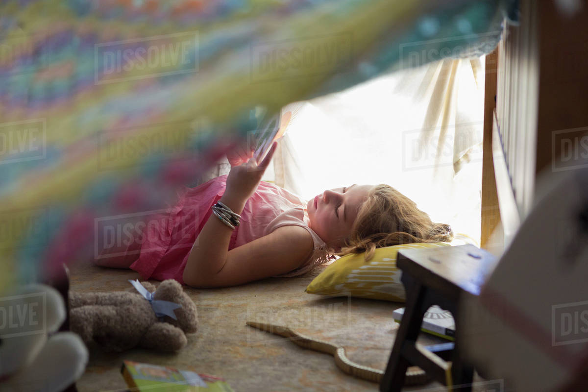 Caucasian girl reading in blanket fort Stock Photo Dissolve