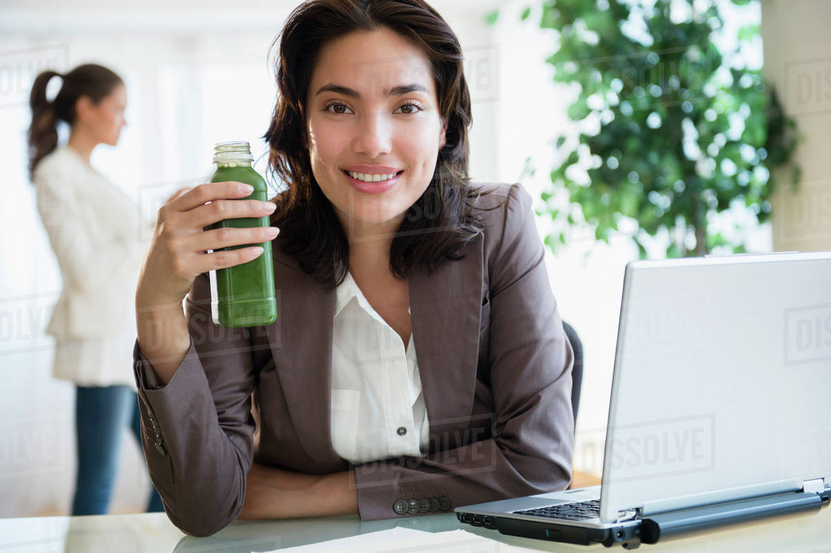 Hispanic businesswoman drinking green juice at desk in office Stock