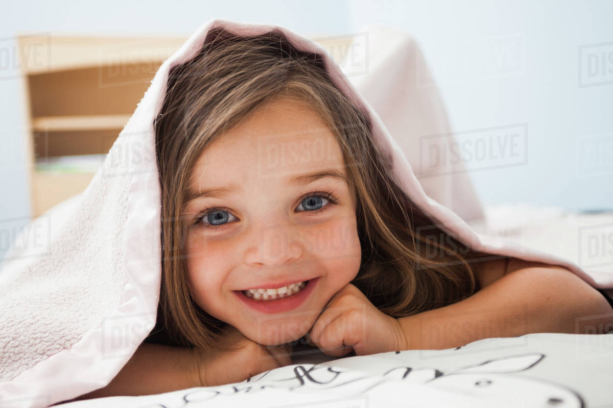 Caucasian girl smiling under covers Stock Photo Dissolve
