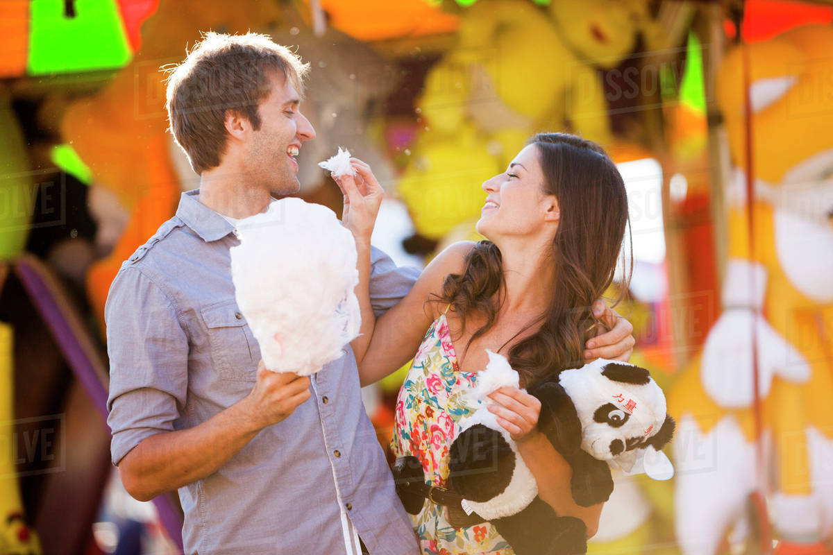 Caucasian couple sharing cotton candy at carnival Stock Photo Dissolve