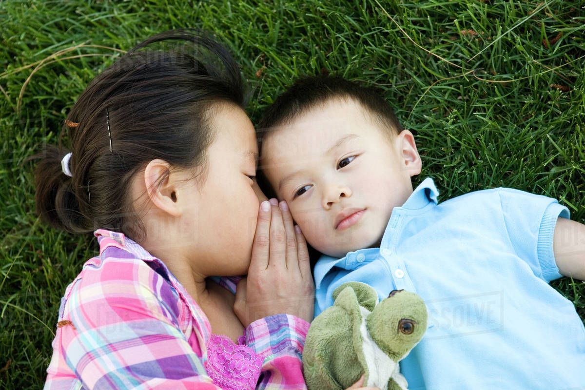 Chinese girl laying in grass and whispering to brother Stock Photo