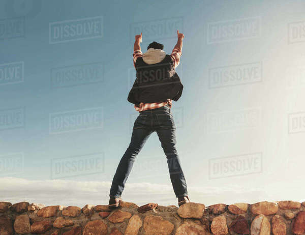 Rear view of man on road trip standing on the embankment with his arms ...