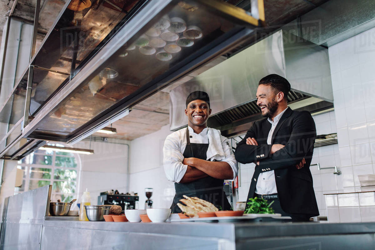 Smiling restaurant owner and chef standing in kitchen. Businessman with
